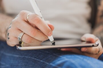Person with rings and tattoos uses stylus to draw or write on a digital tablet © SKILLTAKES.COM