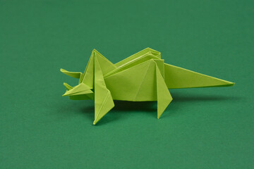 A handmade green paper origami triceratops dinosaur stands on a dark green surface in a studio shot