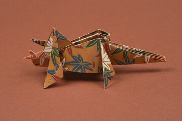 A single handmade paper origami triceratops with a brown and blue floral pattern stands on a solid brown surface in a studio shot