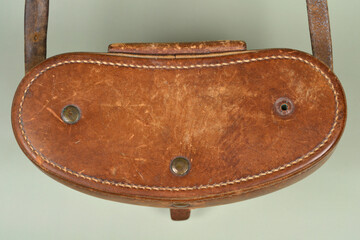 Top view of the oval lid of a weathered brown leather binoculars case showing detailed stitching and metal rivets on a neutral background