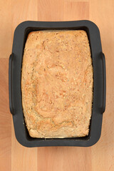 Top view of a loaf of freshly baked homemade whole grain bread sitting in a black silicone baking mold on a wooden table surface