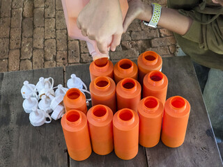 Close up of hand pouring material into bright orange plastic bottle on wooden workbench. focused scene of manufacturing and assembly showing manual labor and precision