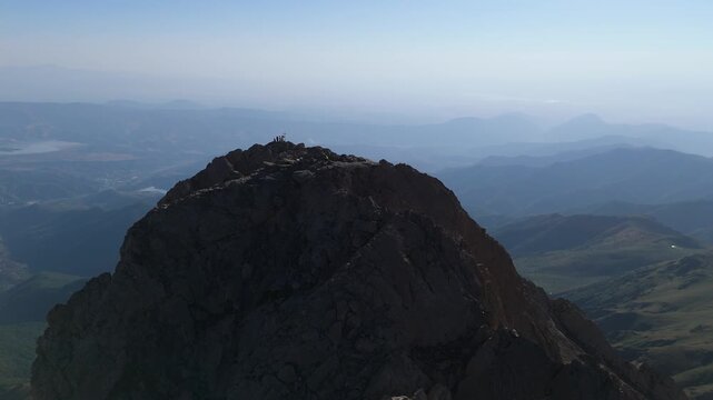 Mount Khustup in Syuniq province, Armenia. People are hiking up a mountain to reach the summit. The sun is rising, and the landscape shows vast mountains and valleys. The air is clear and fresh. Touri