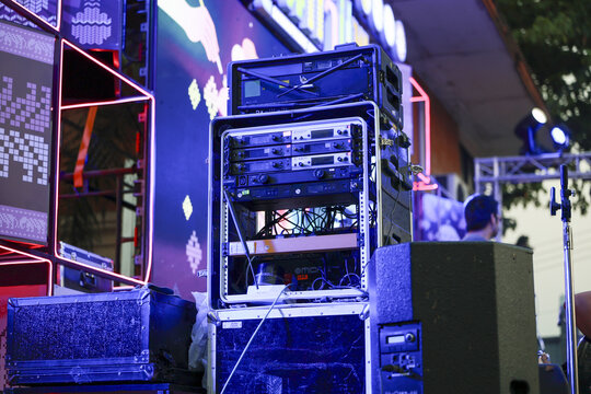 Blue stage lighting illuminates professional sound system with speaker, amplifier, and equipment rack for an energetic outdoor music festival or night concert celebration
