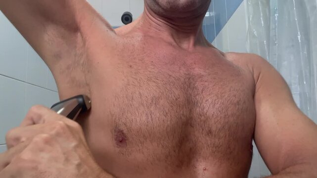 Close-up of an adult man shaving armpit hair in a bathroom, showing male grooming, personal hygiene, and daily self-care routine at home