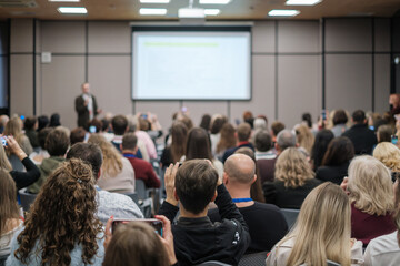 Business conference scene, diverse audience listens to speaker and screen presentation, professional networking and learning.