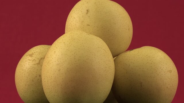 Speckled yellow Asian pears rotate in close up on red background