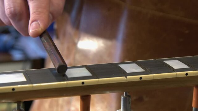 Closeup guitar tech widens ebony fretboard slots on electric guitar