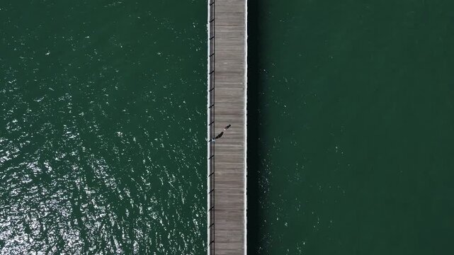 People walk the must-see tourist attraction the Urangan Pier in Hervey Bay a historic timber jetty extending out into the coral sea. Drone view