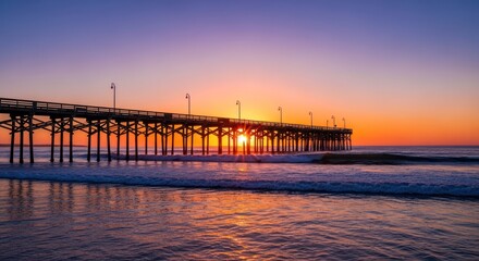 A wooden pier extends into the ocean at sunrise, casting long shadows with a vibrant sky