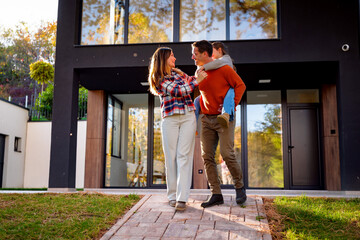 Happy family, parents and child, walking on the paved pathway in front of their modern dream house,...