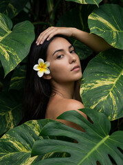 Young woman with flower in hair surrounded by tropical leaves  