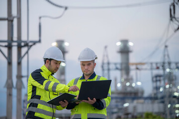 Fototapeta premium Professional engineers using a digital tablet at a petrochemical refinery or oil and gas power plant during twilight. Concept of energy industry, petroleum infrastructure, and industrial teamwork.