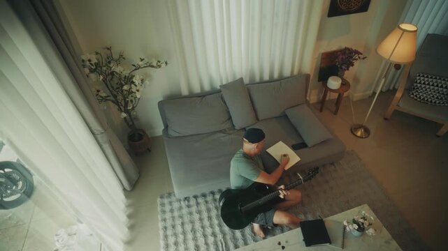 Man Creating Music. Person Sitting Barefoot Crafting Tunes With Acoustic Guitar And Notebook