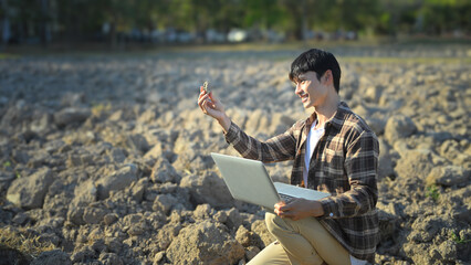 Farmer analyzing soil sample with laptop in dry field