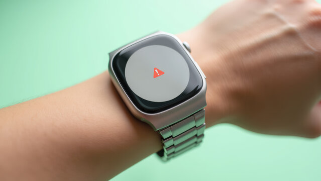 Smartwatch with metal band displaying warning symbol on screen, modern wearable technology, closeup on wrist, green background