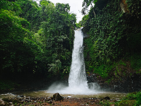 Tropical waterfall cascading into a rocky river surrounded by lush green forest in East Java, Indonesia