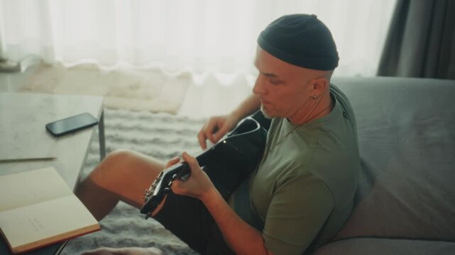 Man Adjusting Guitar Comfortably Indoors. Casual Musician Finetuning Strings In Relaxed Environment