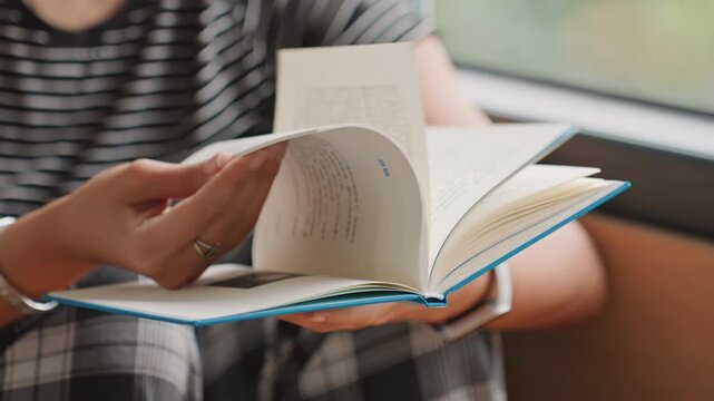 Book page interaction. Detailed view of hand turning book pages. Focus on fingertips and binding during reading session. Intimate shot capturing tactile process of reading in hotel setting