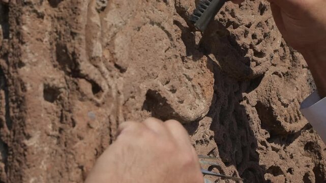 Close-up of an archaeologist cleaning ancient stone carvings with a brush and spatula, steady shot.
