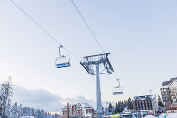 Ski lift chairs ascending over snowy resort at dusk.