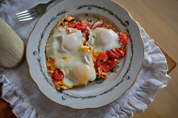 Traditional fried eggs with tomatoes served on a vintage floral plate.