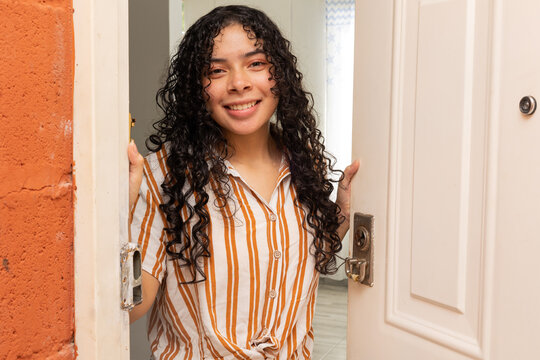 Young woman opening the door with a smile and welcoming gesture. Concept of welcome, hospitality, trust, and lifestyle at home