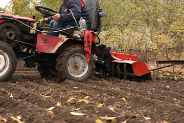 Obraz premium Man on red tractor plowing the field from side, medium shot, plow lowered into soil, horizontal shot.