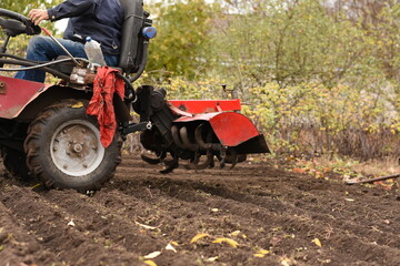Obraz premium Man on red tractor, side view, close-up of rear part, plow lifted above soil, horizontal shot.