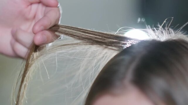 Close up of a professional hairdresser using a black comb to section and lift blonde hair during a salon styling session
