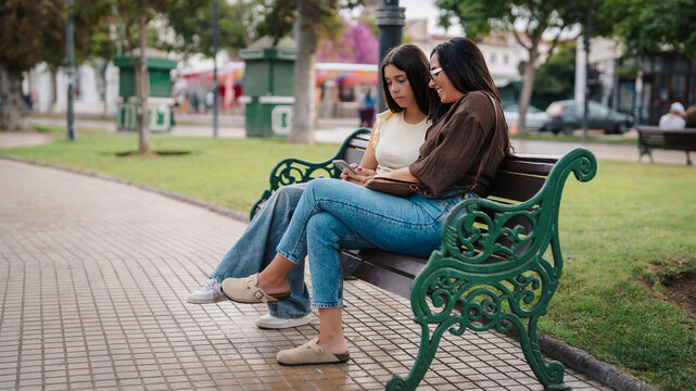 Mother and daugther sitting on a park bench, connecting through a smartphone