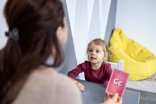 Speech therapist working with a young child using a c letter flashcard, assisting with speech development, learning, and communication skills in an educational setting