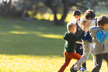 Obraz premium Happy boys playing together, chasing bubbles in park
