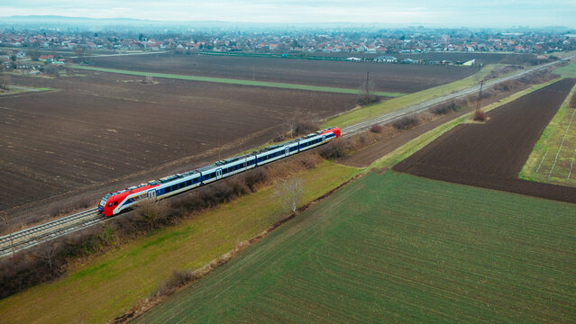 Aerial view of a train slicing through the landscape, contrasting the earthy browns of plowed fields with the vibrant greens of growing crops, Novi Sad, Vojvodina, Serbia.