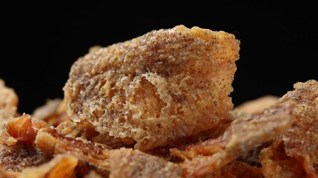 Pile of crispy fried boneless gourami fish fillets pieces rotating slowly on black background. Thai food