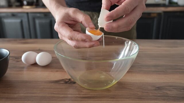 Mans hands cracking eggs into bowl to separate yolks from whites for sponge cake batter. Baking preparation and precise culinary technique.