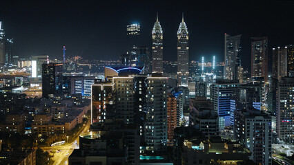 Naklejka premium Dubai by night, city skyline with The Business Central Towers, illuminated highways, and modern glass and steel skyscrapers, aerial view.