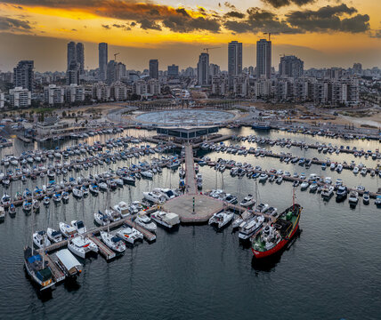 Aerial view of yachts clustered tightly in the marina, framed by the city skyline during a fiery sunset, Ashdod, South District, Israel.