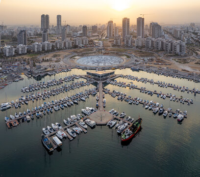 Aerial view of boats nestled in the marina water, reflecting the golden hues of the sunset, against the backdrop of the city skyline, Ashdod, South District, Israel.