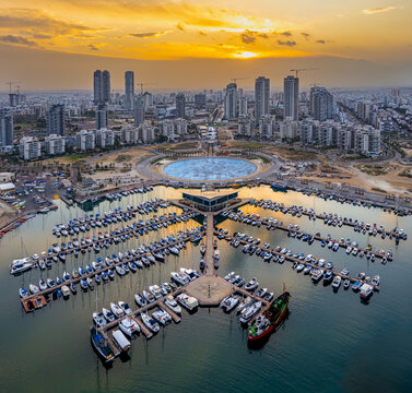 Aerial view of boats docked near the marina, contrasting with the city skyline under a vibrant sunset, Ashdod, South District, Israel.