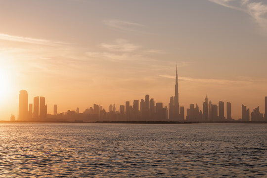 Sunset city skyline view from Dubai Creek Harbor, futuristic skyscrapers and vibrant desert sunset sky.