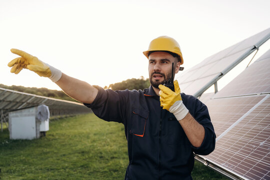 Talking by a walkie talkie. Male solar engineer examining photovoltaic panels at a power station
