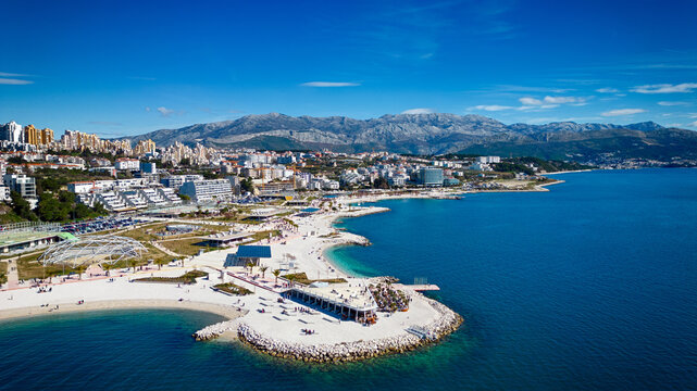 Aerial view of the pristine white beach contrasting against the azure waters, backed by the city's modern architecture and distant mountains, Split, Split-Dalmatia County, Croatia.