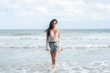 Fototapeta premium Beautiful young woman walking in sea water on tropical beach wearing sunglasses enjoying summer vacation travel