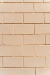 Fototapeta premium Pale yellow plaster wall with an imitation brick pattern forming a clean textured background. Decorative masonry-style surface with rectangular blocks arranged in a regular pattern.