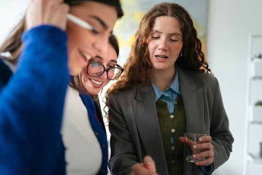 Three women collaborate on a project, one holding a stylus and looking at a screen, while another smiles and the third listens intently.