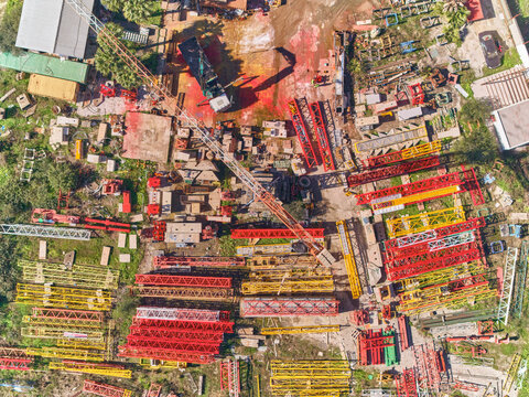 Aerial view of a vibrant crane yard, an array of red and yellow crane parts contrasting against the gritty industrial landscape, Metal Grua, Estepona, Andalusia, Spain.