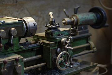 Close up of vintage metal lathe machine with control handles and cutting tool in industrial workshop interior. Precision engineering, mechanical manufacturing and heavy industry equipment.