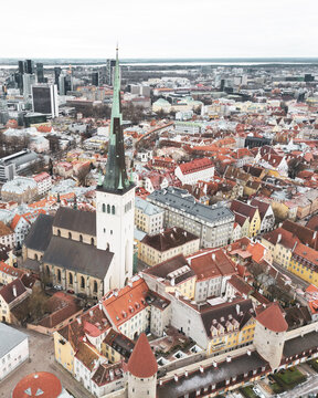Aerial view of St. Olaf's Church spire piercing the skyline amidst a tapestry of orange rooftops and modern high-rises, Tallinn, Harju County, Estonia.