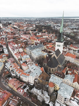 Aerial view of St. Olaf's Church spire pierces the skyline amidst a tapestry of terracotta rooftops and historic buildings, Tallinn, Harju County, Estonia.